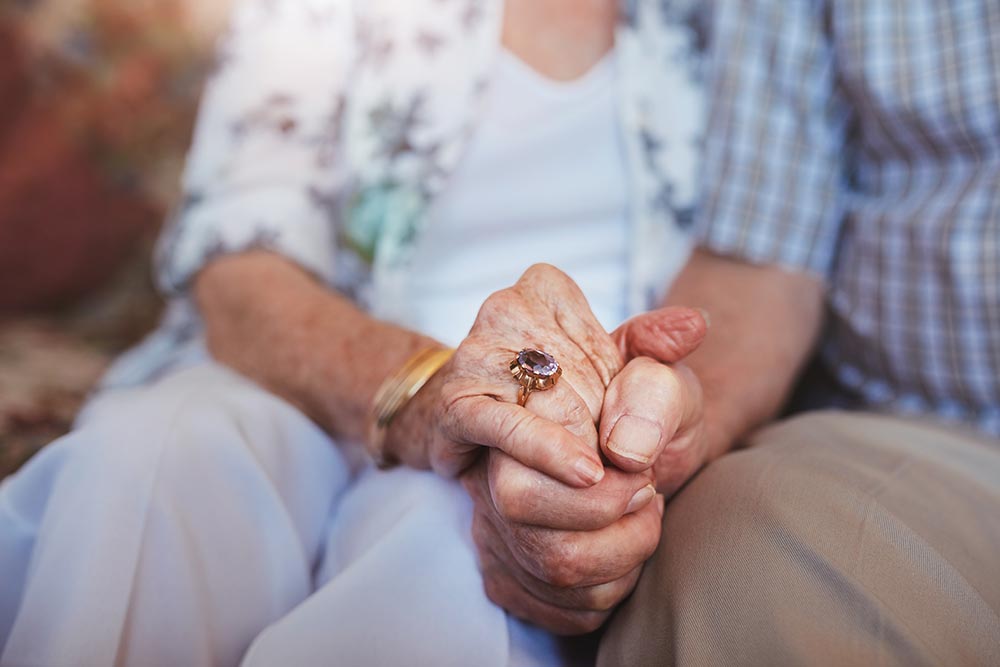 Two elderly people in senior living in Illinois sit closely, holding hands. Two elderly people in senior living in Illinois sit closely, holding hands.